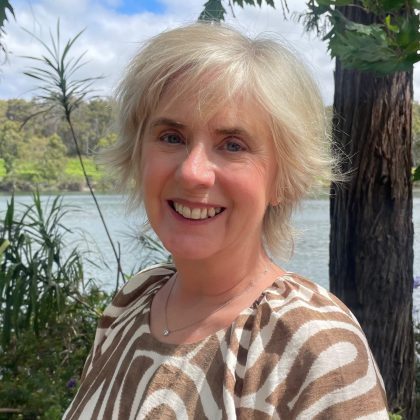 Dr Clare Matthews smiles at the camera in an outdoor setting She has short white hair and is wearing a white and brown patterned top