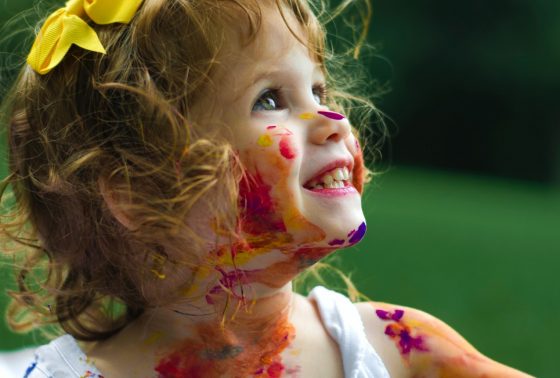 A young girl covered in multi-coloured paint